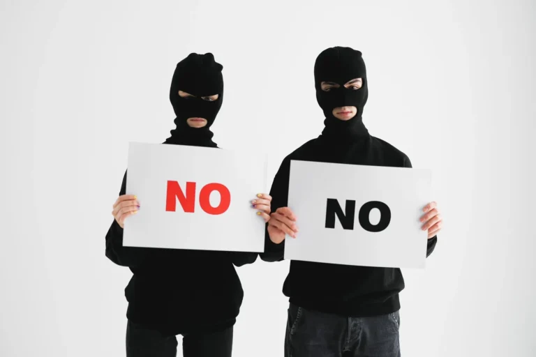 Deux personnes masquées tenant des panneaux “NO” pour illustrer les limites des sites web créés uniquement avec l’intelligence artificielle.