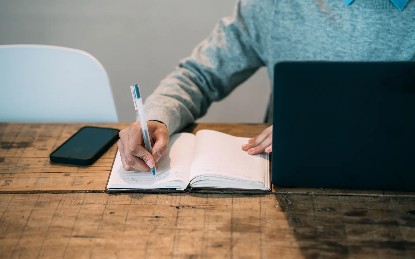 Une personne prend des notes dans un agenda à côté de son ordinateur