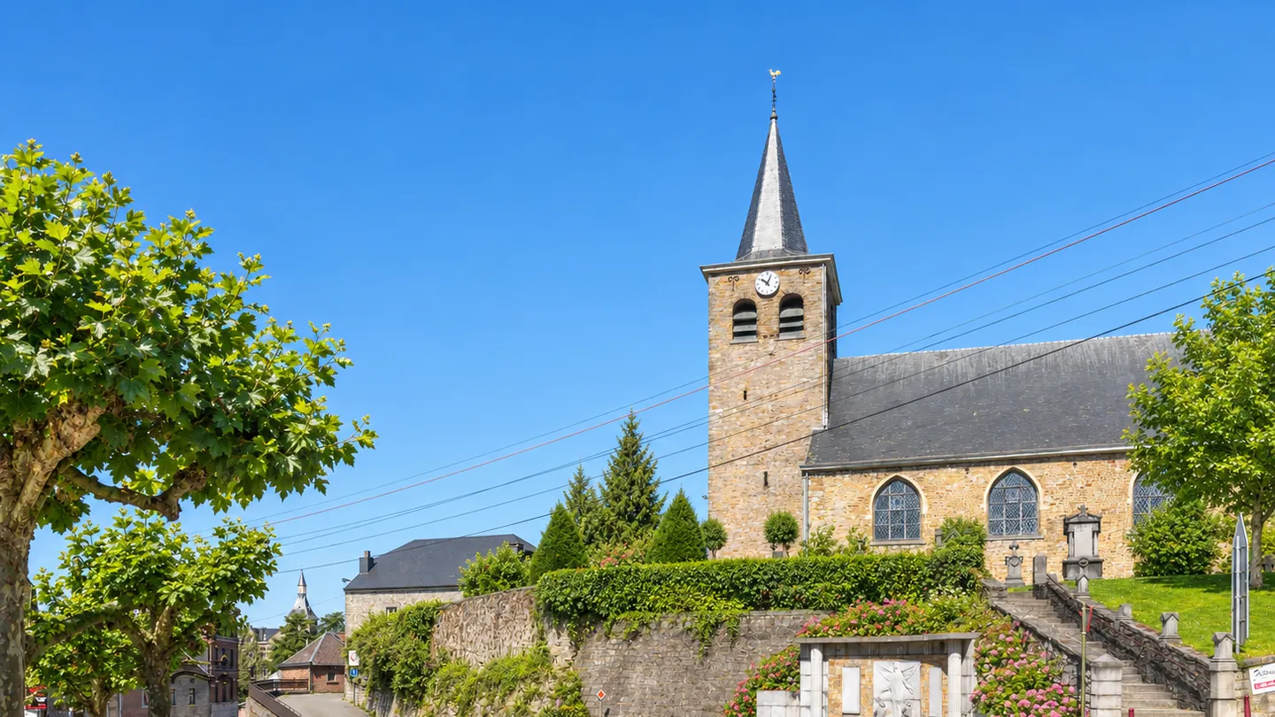 Église Saint-Martin de Sprimont entourée d’arbres et de fleurs en été